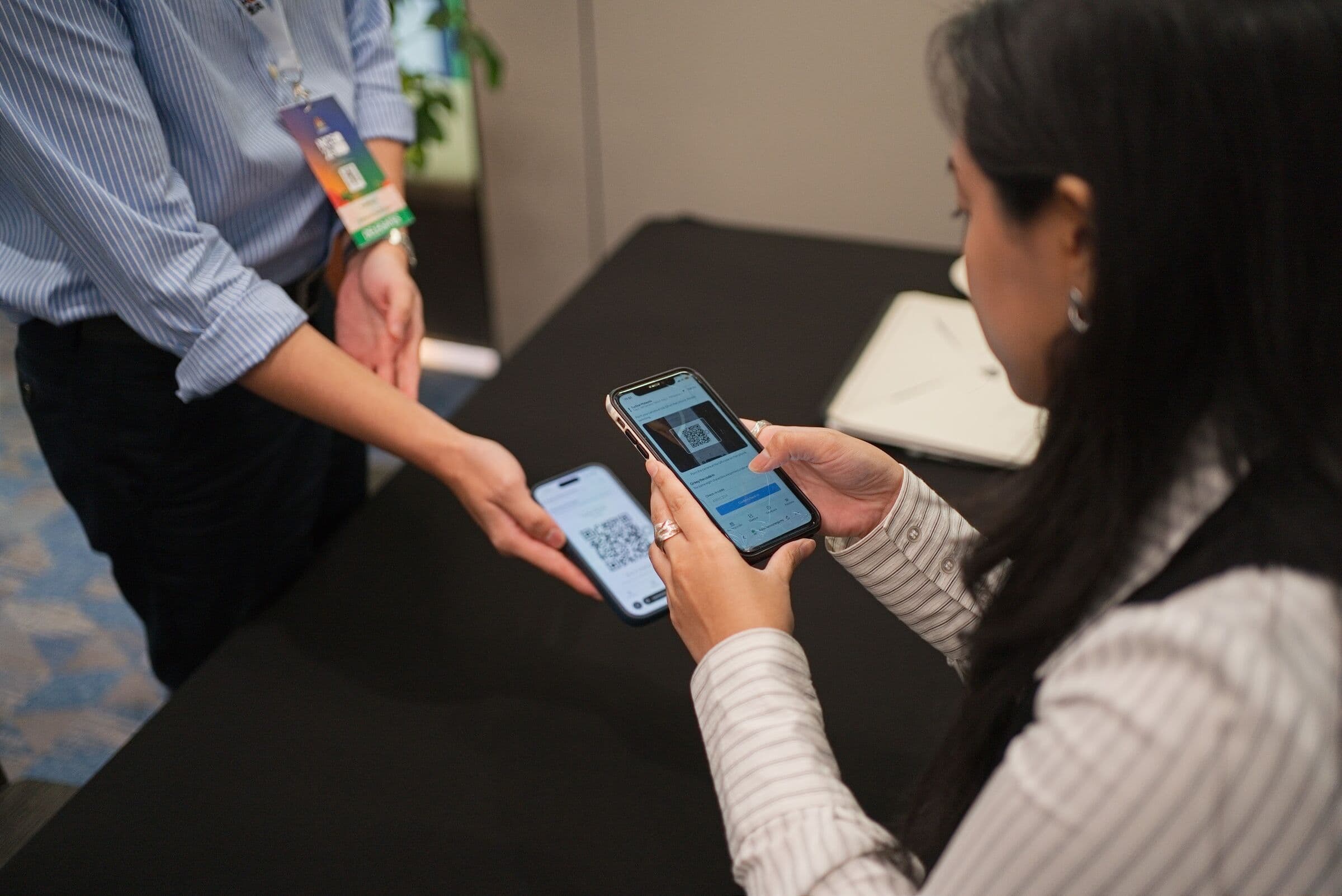 Two attendees showing QR codes on their phones at a check-in table, NICE 2026